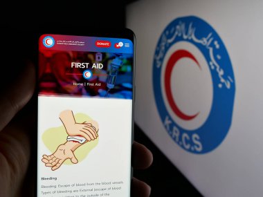 Stuttgart, Almanya - 06-19-2025: Kuveyt Kızılı Hilal Derneği 'nin (KRCS) web sayfası logonun önünde duran kişi. Telefon ekranının merkezine odaklan.