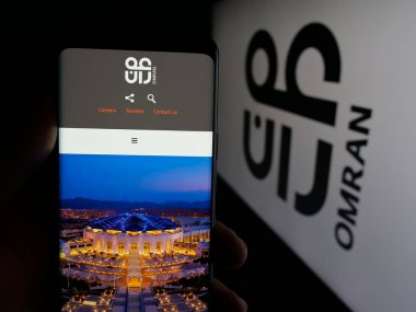 Stuttgart, Almanya - 06-20-2025: Umman Turizm Geliştirme Şirketi 'nin (Omran) web sayfası logonun önünde elinde akıllı telefon bulunan kişi. Telefon ekranının merkezine odaklan.