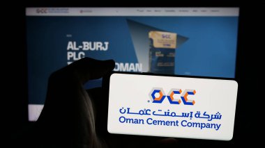 Stuttgart, Almanya - 06-20-2025: İnternet sayfası önünde üzerinde Umman Çimento Şirketi (OCC) logosu bulunan cep telefonu sahibi kişi. Telefon ekranına odaklan.