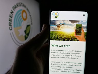 Stuttgart, Almanya - 06-20-2025: Tarım projesi Green Pakistan Initiative 'in web sayfası olan akıllı telefonu logo önünde ekranda tutan kişi. Telefon ekranının merkezine odaklan.