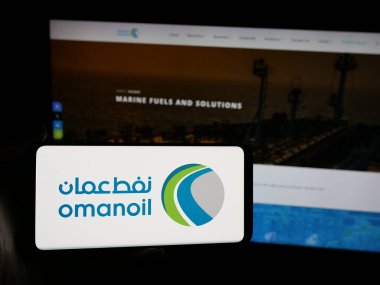 Stuttgart, Almanya - 06-20-2025: İnternet sitesi önünde üzerinde Umman Petrol Pazarlama Şirketi (OOMCO) logosu bulunan akıllı telefon sahibi kişi. Telefon ekranına odaklan.