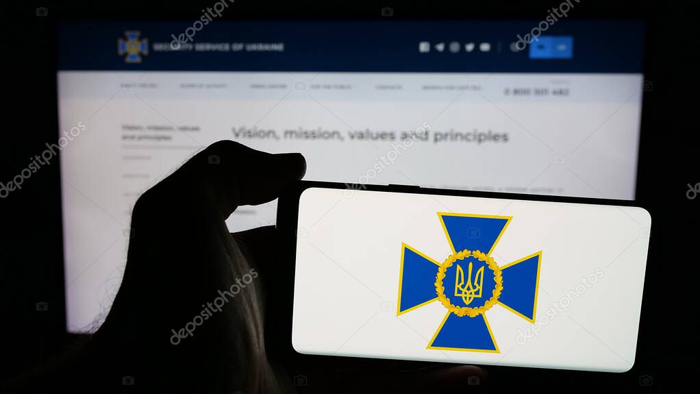 Stuttgart, Germany - 06-18-2025: Person holding mobile phone with logo of security service Sluzhba Bezpeky Ukrainy SBU on screen in front of web page. Focus on phone display.