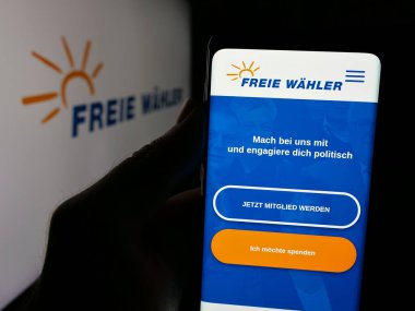 Stuttgart, Almanya - 06-26-2025: Alman siyasi partisinin web sitesi Freie Waehler ile birlikte logonun önünde akıllı telefon tutan kişi. Telefon ekranının merkezine odaklan.