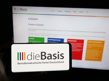 Stuttgart, Almanya - 06-26-2025: Web sitesi önünde üzerinde Alman Basisdemokratische Partei (dieBasis) logosu bulunan akıllı telefon sahibi kişi. Telefon ekranına odaklan.
