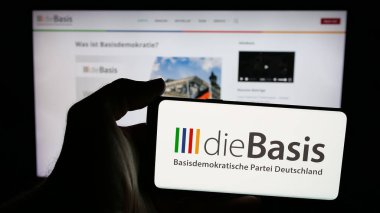 Stuttgart, Almanya - 06-26-2025: İnternet sayfası önünde üzerinde Alman Basisdemokratische Partei (DieBasis) logosu bulunan cep telefonu sahibi kişi. Telefon ekranına odaklan.