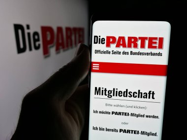 Stuttgart, Almanya - 06-26-2025: Alman siyasi partisinin web sitesi Die PARTEI ile birlikte logo önünde cep telefonu tutan kişi. Telefon ekranının merkezine odaklan.