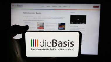 Stuttgart, Almanya - 06-26-2025: İnternet sayfası önünde üzerinde Alman Basisdemokratische Partei (DieBasis) logosu bulunan cep telefonu sahibi kişi. Telefon ekranına odaklan.