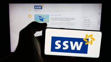 Stuttgart, Almanya - 06-26-2025: İnternet sayfası önünde üzerinde Alman Suedschleswigscher Whaelerbandı (SSW) logosu olan cep telefonu sahibi kişi. Telefon ekranına odaklan.