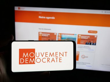 Stuttgart, Almanya - 06-26-2025: İnternet sitesi önünde üzerinde Fransız partisi Mouvement Democrate 'nin (MoDem) logosu bulunan akıllı telefon sahibi kişi. Telefon ekranına odaklan.