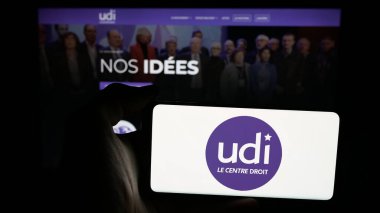 Stuttgart, Almanya - 06-26-2025: Web sayfası önünde Union des Democrates et Independants (UDI) logosunun bulunduğu cep telefonu sahibi kişi. Telefon ekranına odaklan.
