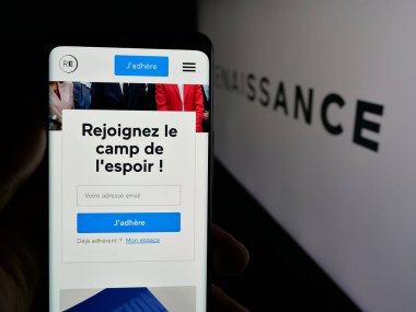 Stuttgart, Almanya - 06-26-2025: Fransız siyasi partisi Rönesans 'ın (RE) web sayfası logonun önünde cep telefonu tutan kişi. Telefon ekranının merkezine odaklan.