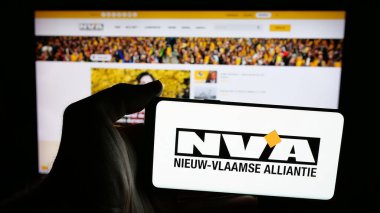 Stuttgart, Almanya - 07-10-2025: İnternet sayfasının önünde Nieuw-Vlaamse Alliantie (N-VA) adlı Belçika partisinin logosunu elinde tutan kişi. Telefon ekranına odaklan.