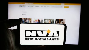Stuttgart, Almanya - 07-10-2025: İnternet sayfasının önünde Nieuw-Vlaamse Alliantie (N-VA) adlı Belçika partisinin logosunu elinde tutan kişi. Telefon ekranına odaklan.