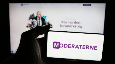 Stuttgart, Almanya - 07-11-2025: İnternet sayfasının önünde Danimarka siyasi partisi Moderaterne 'in (M) logosunu elinde tutan kişi. Telefon ekranına odaklan.