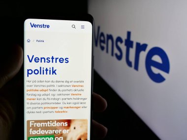 Stuttgart, Almanya - 07-11-2025: Venstre partisinin web sayfası ile cep telefonu tutan kişi - Danimarka Liberal Parti (V) logonun önünde ekranda. Telefon ekranının merkezine odaklan.