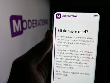 Stuttgart, Almanya - 07-11-2025: Danimarka siyasi partisi Moderaterne 'in (M) web sayfası logonun önünde akıllı telefon tutan kişi. Telefon ekranının merkezine odaklan.