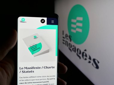 Stuttgart, Almanya - 07-11-2025: Belçika siyasi partisi Les Engages 'in (LE) web sayfası logonun önünde elinde akıllı telefon tutan kişi. Telefon ekranının merkezine odaklan.