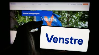 Stuttgart, Almanya - 07-11-2025: Venstre partisinin logosunu taşıyan cep telefonu sahibi kişi - Danmarks Liberale Parti (V) web sayfasının önünde ekranda. Telefon ekranına odaklan.