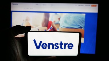 Stuttgart, Almanya - 07-11-2025: Venstre partisinin logosunu taşıyan cep telefonu sahibi kişi - Danmarks Liberale Parti (V) web sayfasının önünde ekranda. Telefon ekranına odaklan.