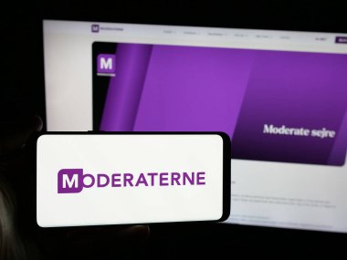 Stuttgart, Almanya - 07-11-2025: İnternet sitesinin önünde Danimarkalı siyasi parti Moderaterne 'in (M) logosunu elinde tutan kişi. Telefon ekranına odaklan.