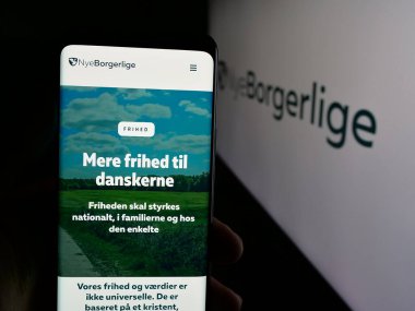 Stuttgart, Almanya - 07-11-2025: Danimarka siyasi partisi Nye Borgerlige 'in (NB) web sayfası logonun önünde cep telefonu tutan kişi. Telefon ekranının merkezine odaklan.