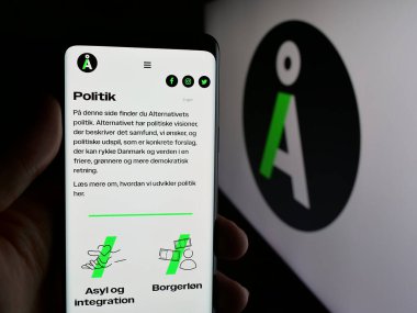 Stuttgart, Almanya - 07-11-2025: Danimarka siyasi partisi Alternativet 'in (A) web sayfası logonun önünde bulunan kişi. Telefon ekranının merkezine odaklan.