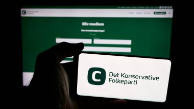 Stuttgart, Almanya - 07-11-2025: Danimarkalı partinin logosu Det Konservative Folkeparti (KF) ile cep telefonu sahibi kişi web sayfası önünde ekranda. Telefon ekranına odaklan.