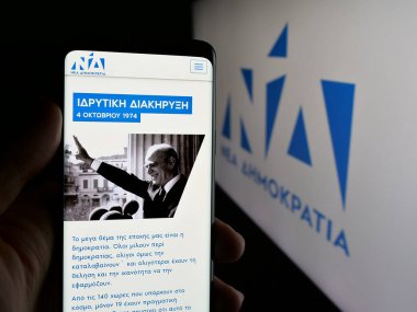 Stuttgart, Almanya - 07-18-2025: Yunan siyasi partisi Nea Dimokratia 'nın (ND) web sayfası logonun önünde duran kişi. Telefon ekranının merkezine odaklan.