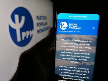 Stuttgart, Almanya - 07-18-2025: Partili Popüler Monarquico 'nun (PPM) web sayfası logonun önünde bulunan kişi. Telefon ekranının merkezine odaklan.