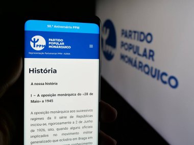 Stuttgart, Almanya - 07-18-2025: Partili Partili Popüler Monarquico 'nun (PPM) web sayfası logonun önünde duran kişi. Telefon ekranının merkezine odaklan.