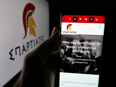 Stuttgart, Almanya - 07-21-2025: Yunan siyasi partisi Spartiates 'in web sayfası logonun önünde duran kişi. Telefon ekranının merkezine odaklan.