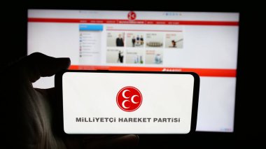 Stuttgart, Almanya - 07-21-2025: Milliyetci Hareket Partisi (MHP) logosunun bulunduğu cep telefonu sahibi kişi web sayfası önünde ekranda. Telefon ekranına odaklan.