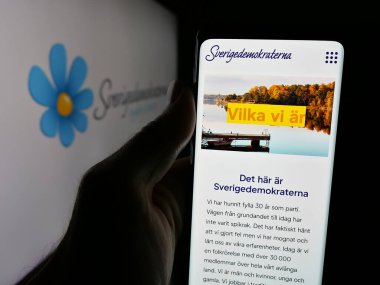 Stuttgart, Almanya - 07-23-2025: İsveç partisi Sverigedemokraterna 'nın (SD) web sayfası logonun önünde duran kişi. Telefon ekranının merkezine odaklan.