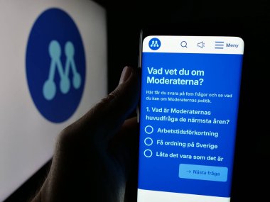 Stuttgart, Almanya - 07-24-2025: Parti Moderata Samlingspartiet 'in (Moderaterna) web sayfası logonun önünde duran kişi. Telefon ekranının merkezine odaklan.