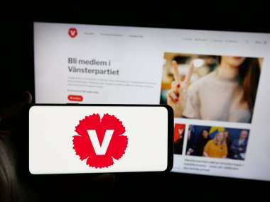 Stuttgart, Almanya - 07-24-2025: İsveçli siyasi parti Vansterpartiet 'in logosunu elinde tutan kişi web sitesinin önünde ekranda. Telefon ekranına odaklan.