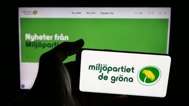 Stuttgart, Almanya - 07-24-2025: İnternet sayfası önünde üzerinde İsveç partisi Miljopartiet de Grona 'nın logosu bulunan cep telefonu sahibi kişi. Telefon ekranına odaklan.