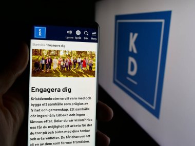 Stuttgart, Almanya - 07-24-2025: İsveç partisi Kristdemokraterna 'nın (KD) web sayfası logonun önünde duran kişi. Telefon ekranının merkezine odaklan.
