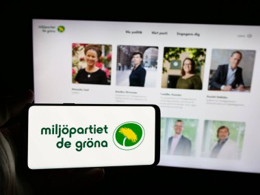 Stuttgart, Almanya - 07-24-2025: İnternet sitesi önünde üzerinde İsveç partisi Miljopartiet de Grona 'nın (MP) logosu bulunan akıllı telefon sahibi kişi. Telefon ekranına odaklan.