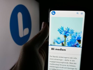 Stuttgart, Almanya - 07-24-2025: İsveç siyasi partisi Liberalerna 'nın internet sayfası logonun önünde duran kişi. Telefon ekranının merkezine odaklan.