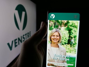 Stuttgart, Almanya - 07-24-2025: Norveç siyasi partisi Venstre 'nin web sayfası logonun önünde duran kişi. Telefon ekranının merkezine odaklan.