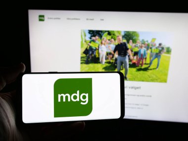 Stuttgart, Almanya - 07-24-2025: Web sitesinin önünde üzerinde Norveç partisi Miljopartiet De Gronne 'un (MDG) logosu bulunan kişi. Telefon ekranına odaklan.