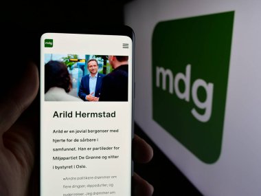 Stuttgart, Almanya - 07-24-2025: Norveç partisi Miljopartiet De Gronne 'un (MDG) web sayfası logonun önünde duran kişi. Telefon ekranının merkezine odaklan.