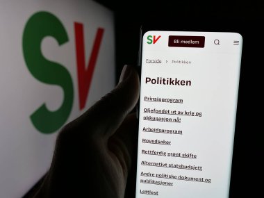Stuttgart, Almanya - 07-24-2025: Sosialistisk Venstreparti 'nin (SV) web sayfası logonun önünde duran kişi. Telefon ekranının merkezine odaklan.