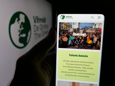 Stuttgart, Almanya - 07-25-2025: Fin siyasi partisi Vihrea Liitto 'nun (Vihreat) internet sayfası logonun önünde duran kişi. Telefon ekranının merkezine odaklan.