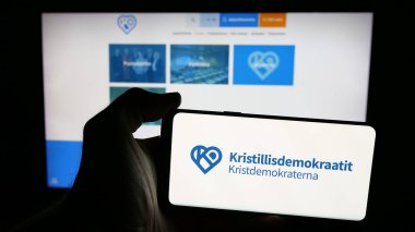 Stuttgart, Almanya - 07-25-2025: İnternet sayfası önünde üzerinde Fin partisi Kristillisdemokraatit (KD) logosu bulunan cep telefonu sahibi kişi. Telefon ekranına odaklan.