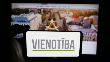 Stuttgart, Almanya - 07-28-2025: Letonya siyasi partisi Vienotiba 'nın logosunun bulunduğu cep telefonu web sayfası önünde ekranda. Telefon ekranına odaklan.
