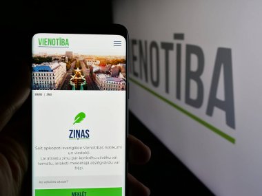 Stuttgart, Almanya - 07-28-2025: Letonya 'nın siyasi partisi Vienotiba' nın web sayfasını elinde tutan kişi logonun önünde ekranda. Telefon ekranının merkezine odaklan.