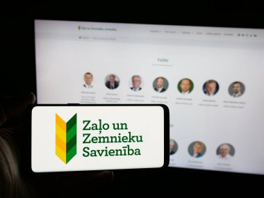 Stuttgart, Almanya - 07-28-2025: İnternet sitesinin önünde Zalo un Zemnieku Savieniba (ZZS) partisinin logosuna sahip akıllı telefon sahibi kişi görülüyor. Telefon ekranına odaklan.