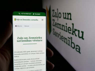 Stuttgart, Almanya - 07-28-2025: Logo önünde Zalo un Zemnieku Savieniba (ZZZS) partisinin web sayfası bulunan kişi. Telefon ekranının merkezine odaklan.