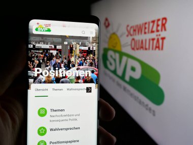 Stuttgart, Almanya - 07-28-2025: İsviçre partisi Schweizerische Volkspartei 'nin (SVP) web sayfası logonun önünde duran kişi. Telefon ekranının merkezine odaklan.